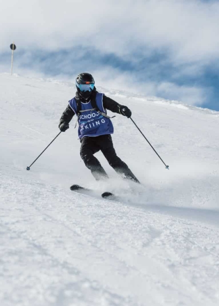 Pupil in a Schools Go Skiing bib carving down a wide piste