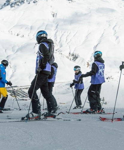 Ski class in Schools Go Skiing bibs lined up on the piste beneath a mountain peak